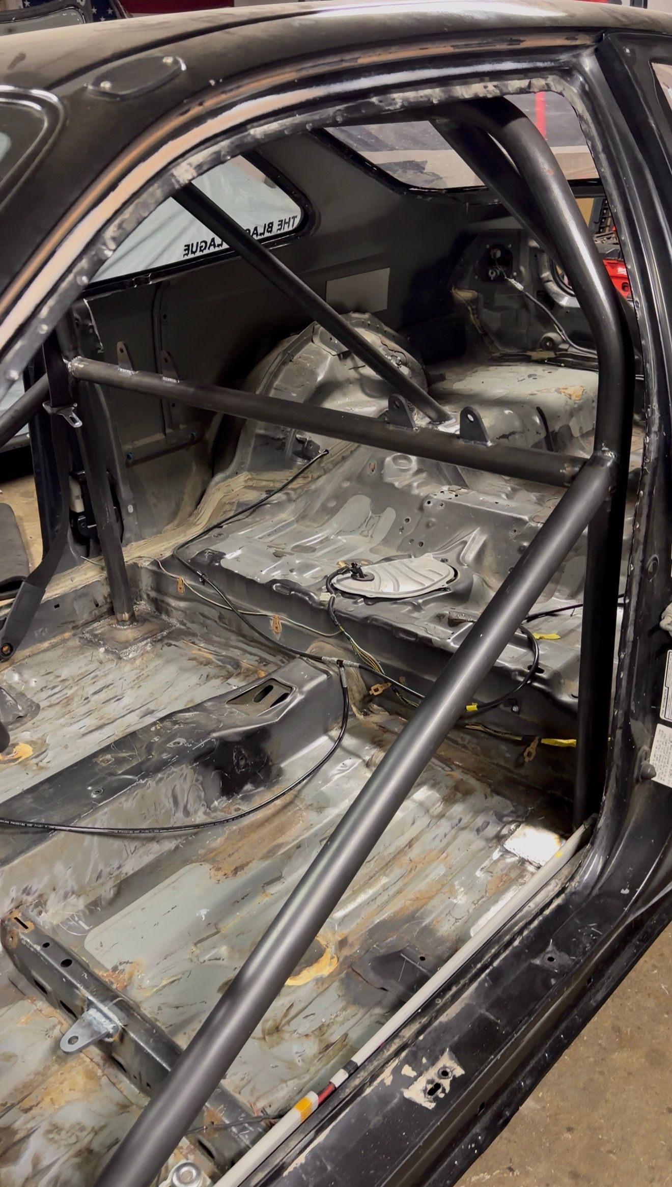 Roll cage tubes inside a stripped black chassis: main hoop, harness bar and a diagonal.